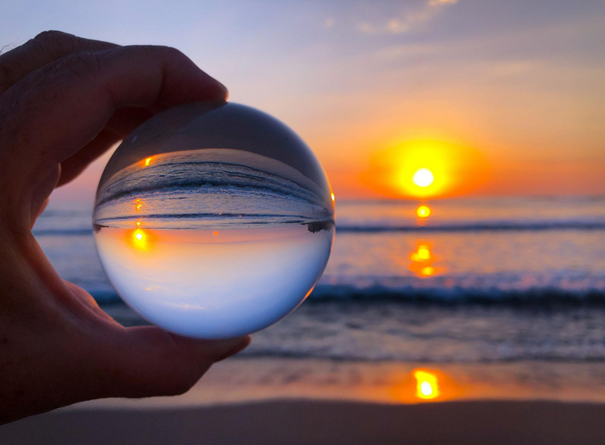 hand holding lens ball showing reversed perspective of sunset and ocean