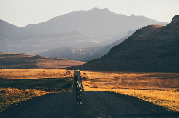 Lone person walking on an empty road toward distant mountains