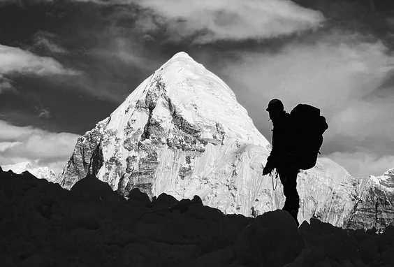 Silhouetted mountaineer with a backpack facing a snow-covered peak