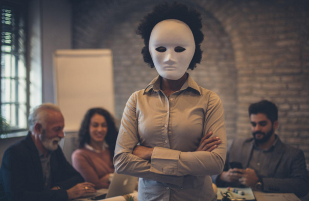 Person in a blank white mask standing with arms crossed during a group meeting